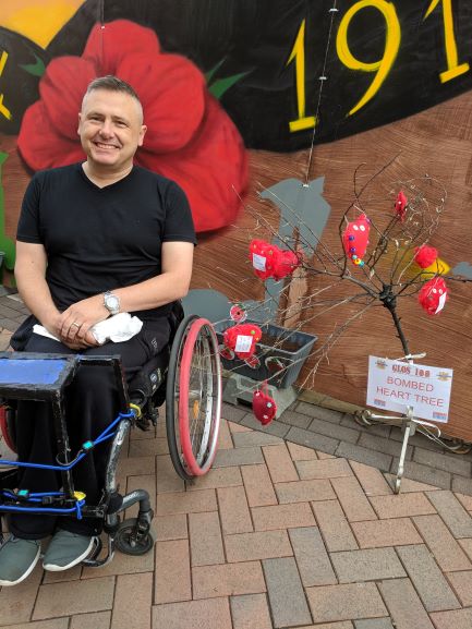 Picture of Chris Auker-Howlett in front of his WW1 Graffiti Wall and Poppy field and burnt out Memorial tree
